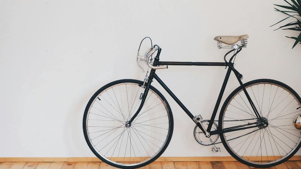 A vintage-style bicycle leaning against a clean white wall with wooden flooring, emphasizing minimalist design.