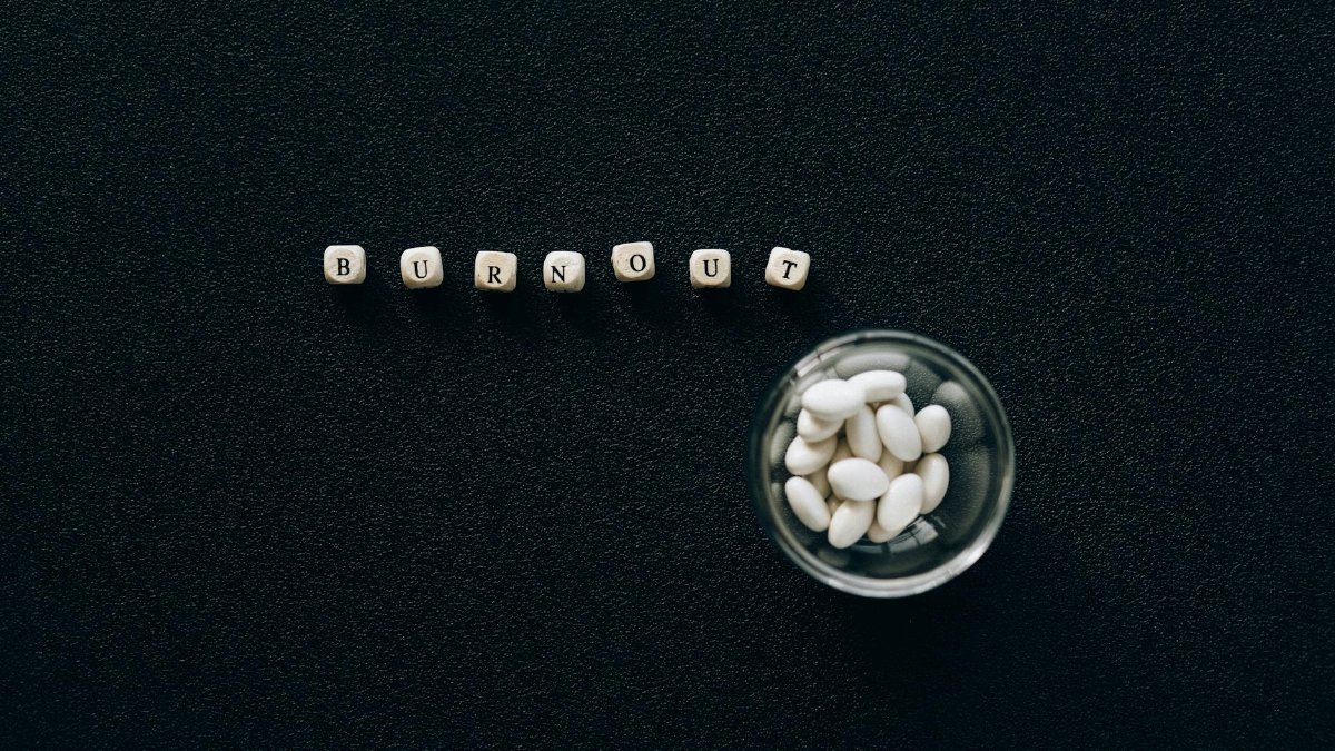 A conceptual image depicting burnout using pills and scrabble tiles on a black surface.