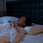 An Asian woman lying awake in bed at night, showing signs of insomnia and sleeplessness.