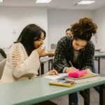 Two female students collaborate in a classroom setting, focusing on their studies.