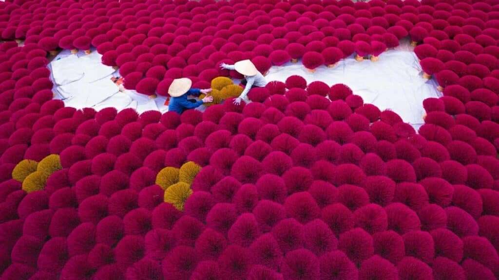 Aerial view of colorful incense sticks being dried outdoors with two workers in traditional hats.