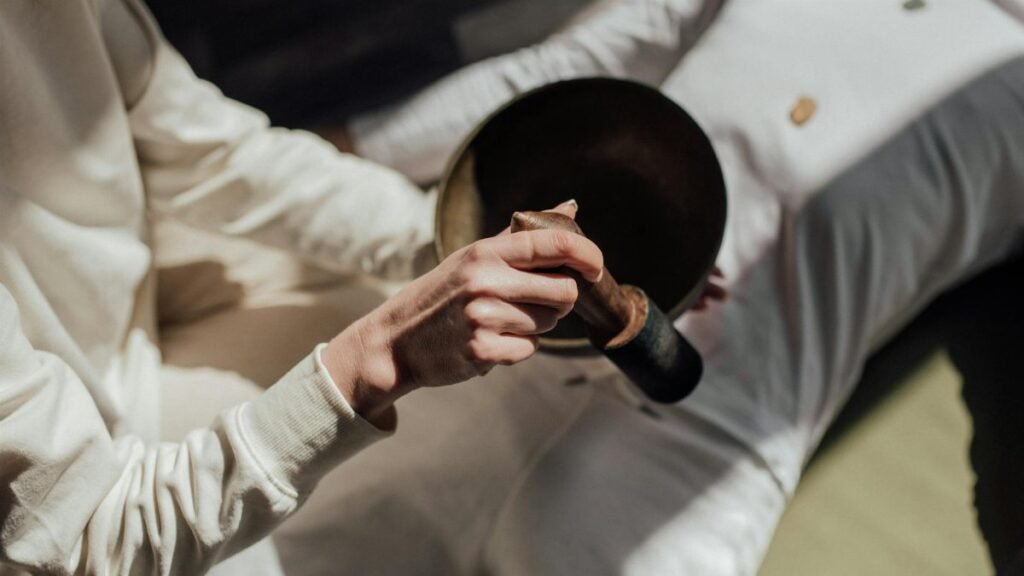 A person using a Tibetan singing bowl for holistic healing and meditation indoors.