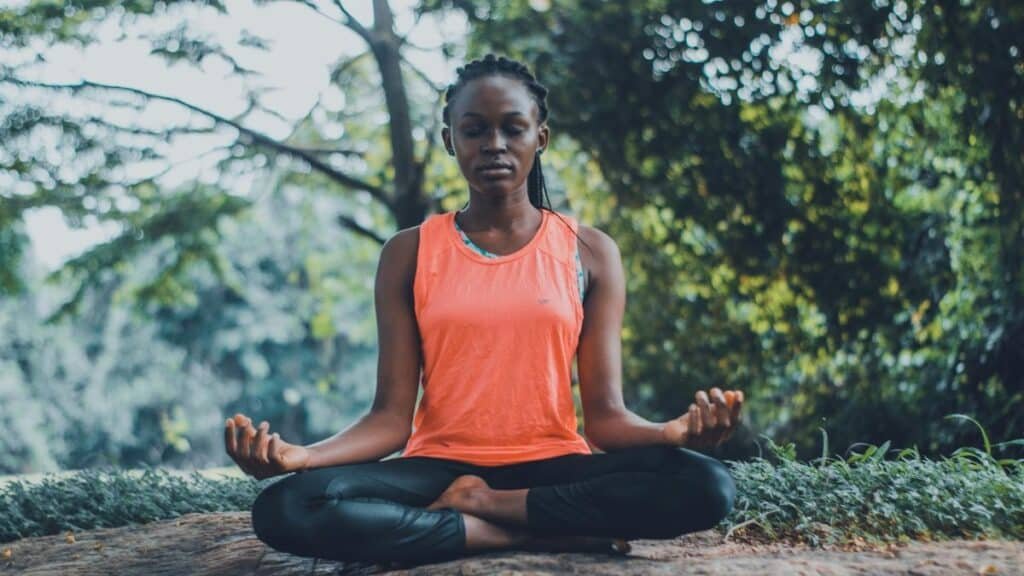 A woman meditating peacefully outdoors in a lush green setting, promoting relaxation and mindfulness.