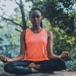 A woman meditating peacefully outdoors in a lush green setting, promoting relaxation and mindfulness.