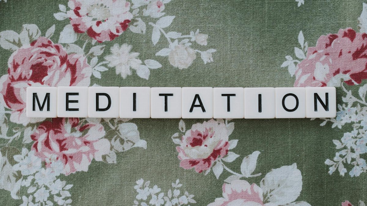 Word 'MEDITATION' spelled with blocks on vintage floral textile background, promoting mindfulness.