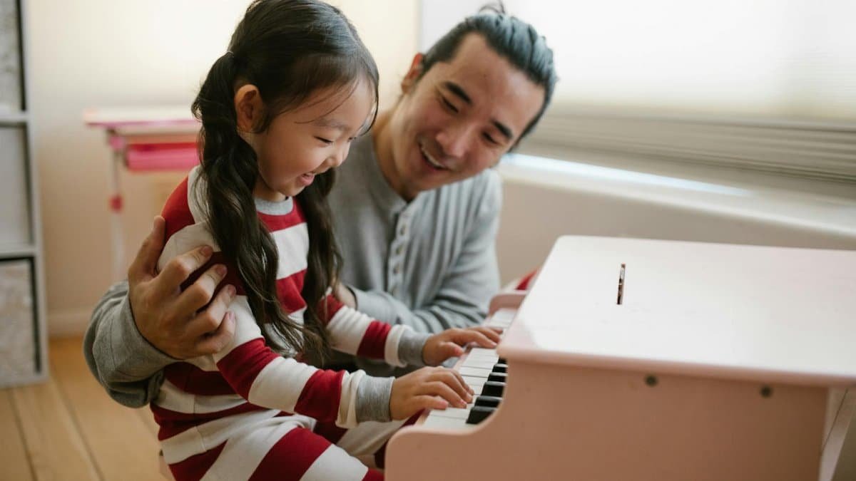 Father and daughter enjoying quality time playing piano together indoors.