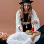 Woman practicing sound healing with singing bowl over another woman. Meditative and relaxing wellness session.