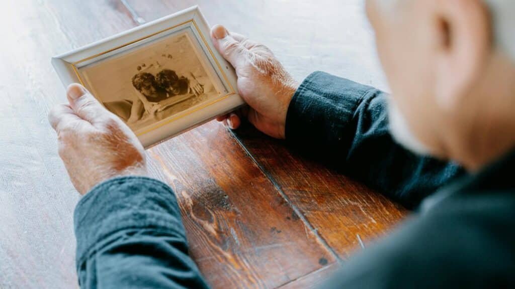 A senior man in black long sleeves holding an old photograph, evoking nostalgia and reflection.