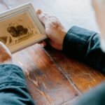 A senior man in black long sleeves holding an old photograph, evoking nostalgia and reflection.