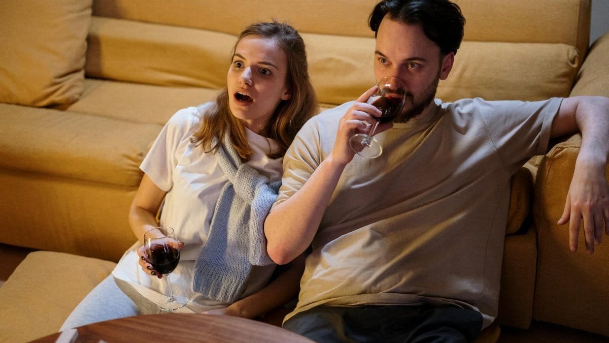 Couple enjoying wine while watching TV, relaxing at home.