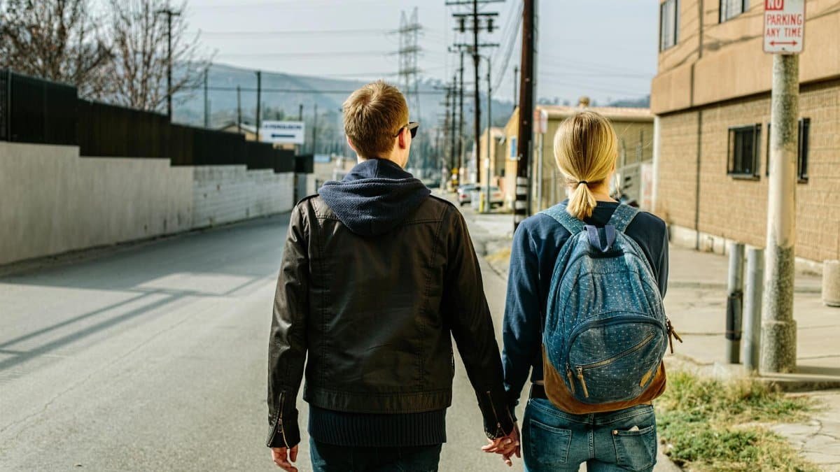 A couple walks hand in hand on an urban street, back view, showcasing companionship and daily life.