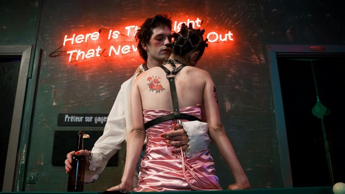 A couple embraces romantically in front of a neon sign at a billiard table in a dimly lit room.