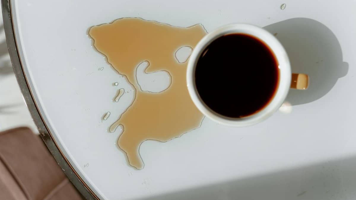 Overhead view of coffee cup and spill on white table with natural lighting.
