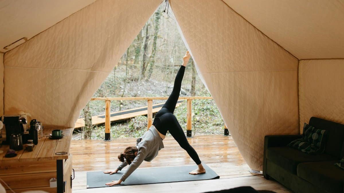 A woman performs yoga inside a glamping tent, surrounded by nature, embodying healthy living and relaxation.