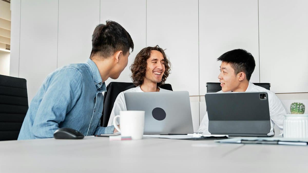 A diverse group of colleagues collaborating in a modern office with laptops and tablets.
