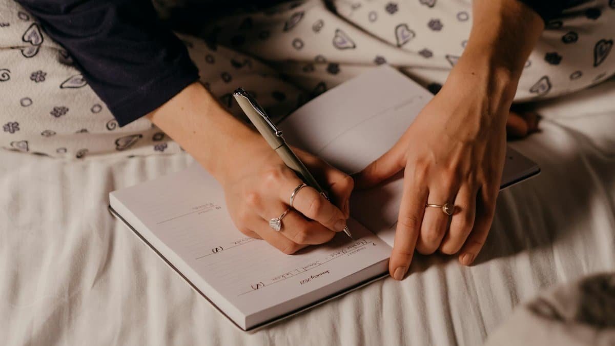 Close-up of a person's hands writing in a journal, showcasing a cozy nighttime ambiance.