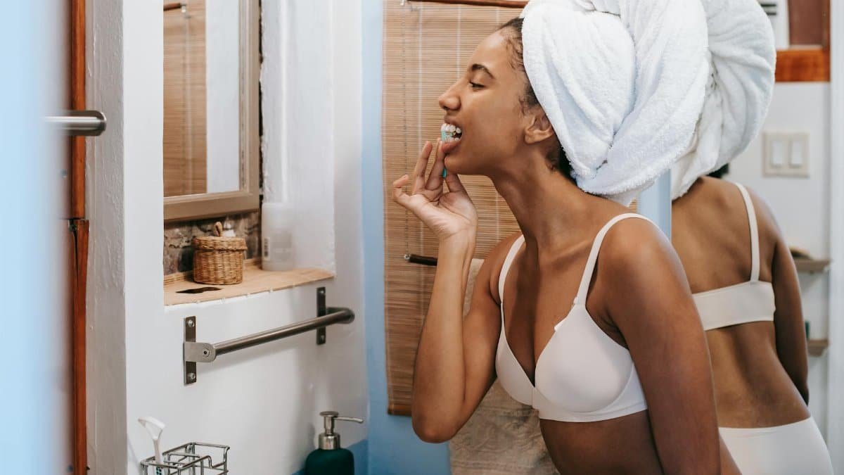 A young woman in a bathroom flossing her teeth with a towel wrapped around her head, promoting oral hygiene.