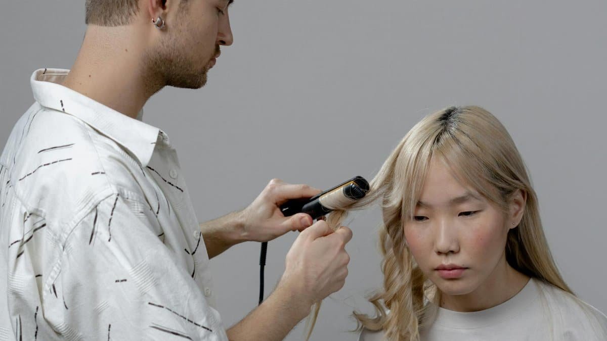 A hairstylist using a curling iron to style a woman's hair in a salon setting.