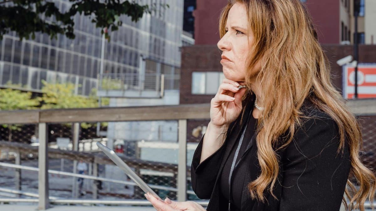 A businesswoman with long hair uses a tablet in an urban setting, showcasing modern technology and business concepts.