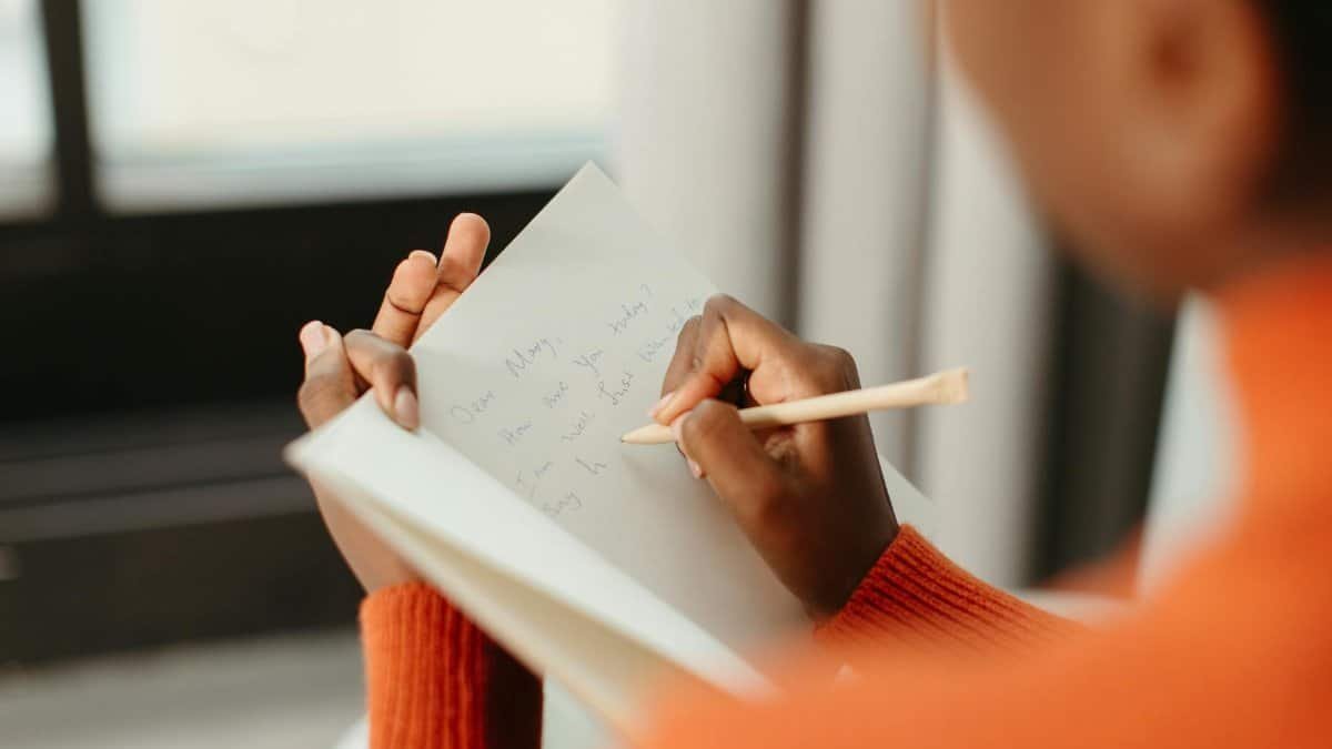 A woman writing a close-up letter in a notebook with a pencil and a blurred background.