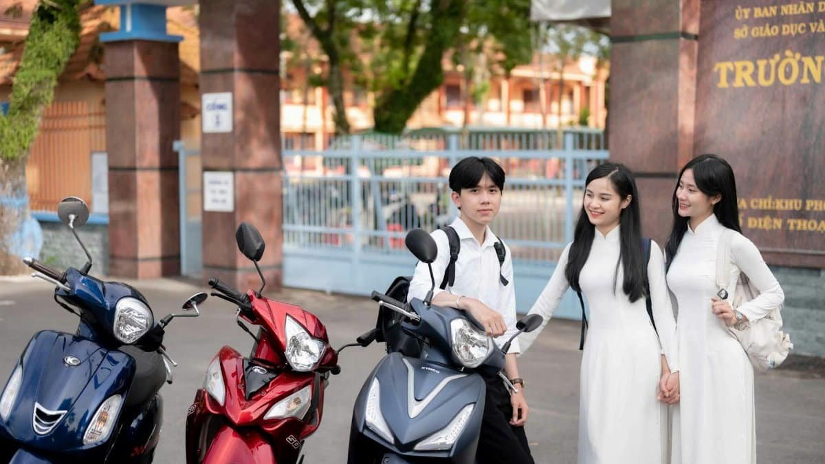 Vietnamese students in traditional attire standing with motorbikes by a school gate in Vietnam.