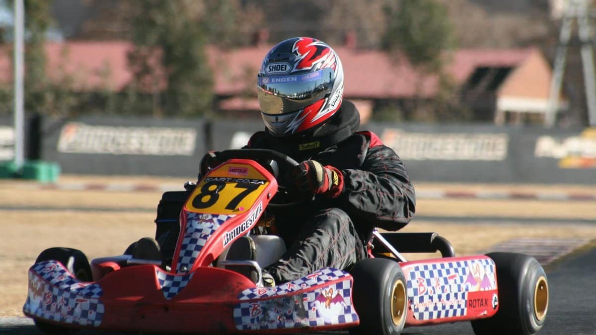 Dynamic photo capturing a go-kart racer speeding at outdoor track in full gear.