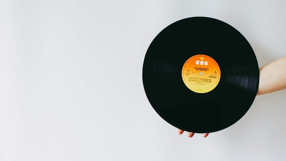 A person's hand holding a classic vinyl record against a solid white background.