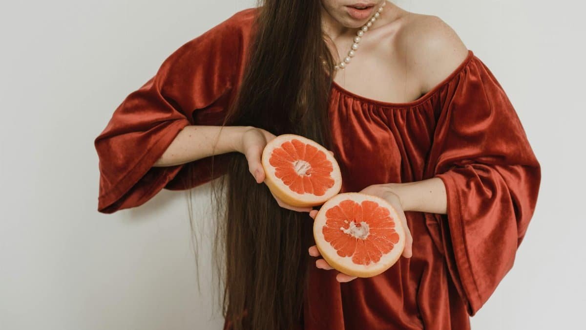A woman in a red dress holds a sliced grapefruit, showcasing fresh citrus fruit.