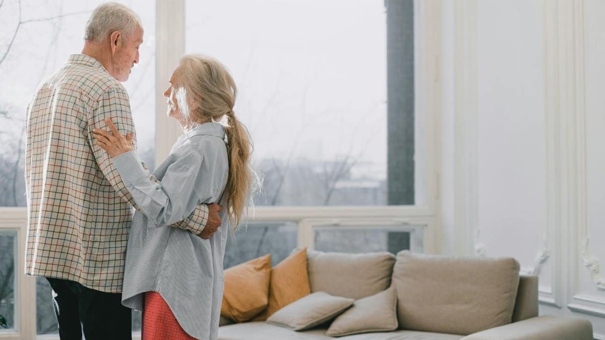 A senior couple shares a tender dance in a bright, cozy living room.