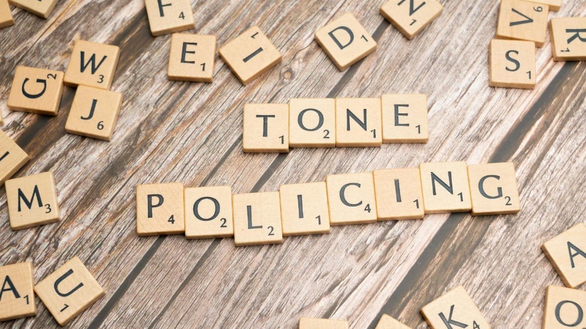 Scrabble tiles spelling 'Tone Policing' arranged on a rustic wooden surface, showcasing communication concepts.