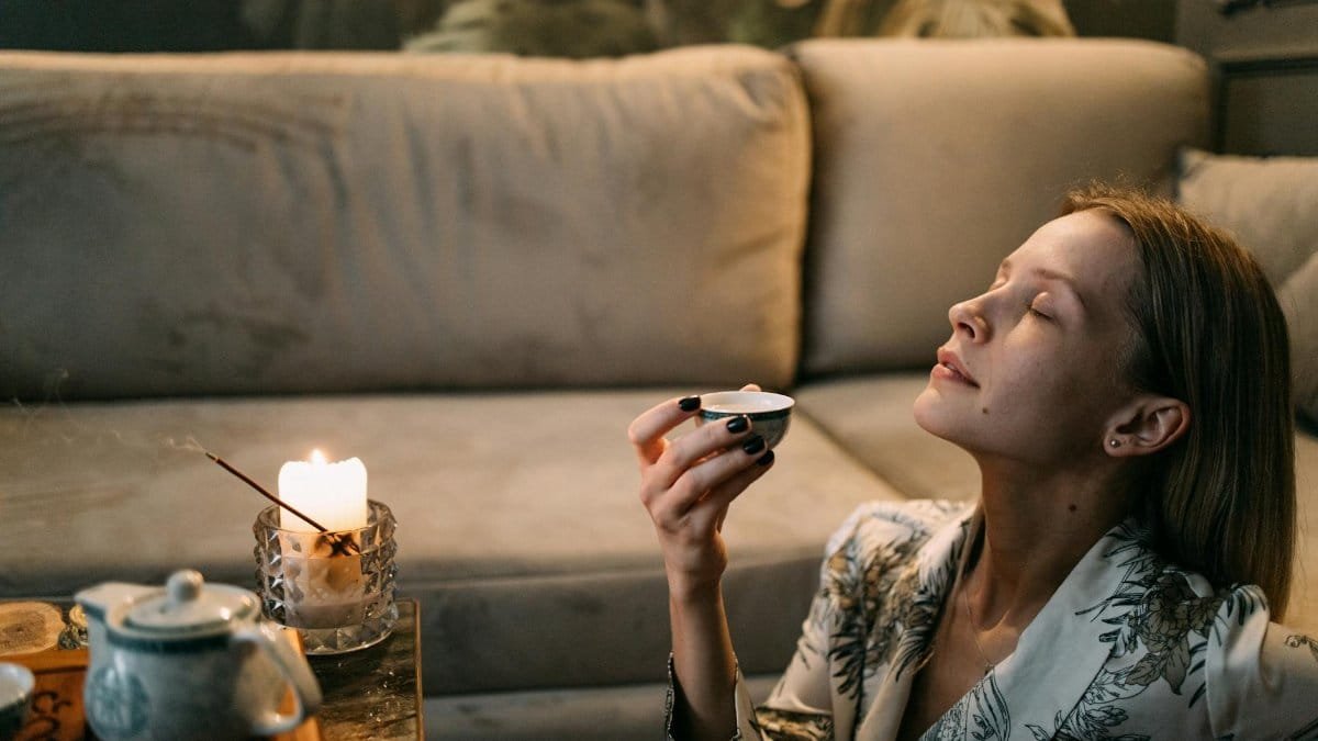 A woman enjoys a relaxing tea ceremony on her sofa with candles and incense.