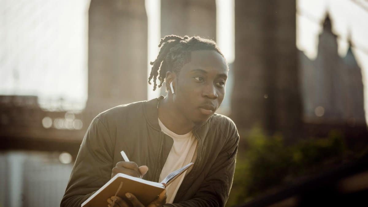 Pensive young man sketching near a famous urban bridge on a sunny day.