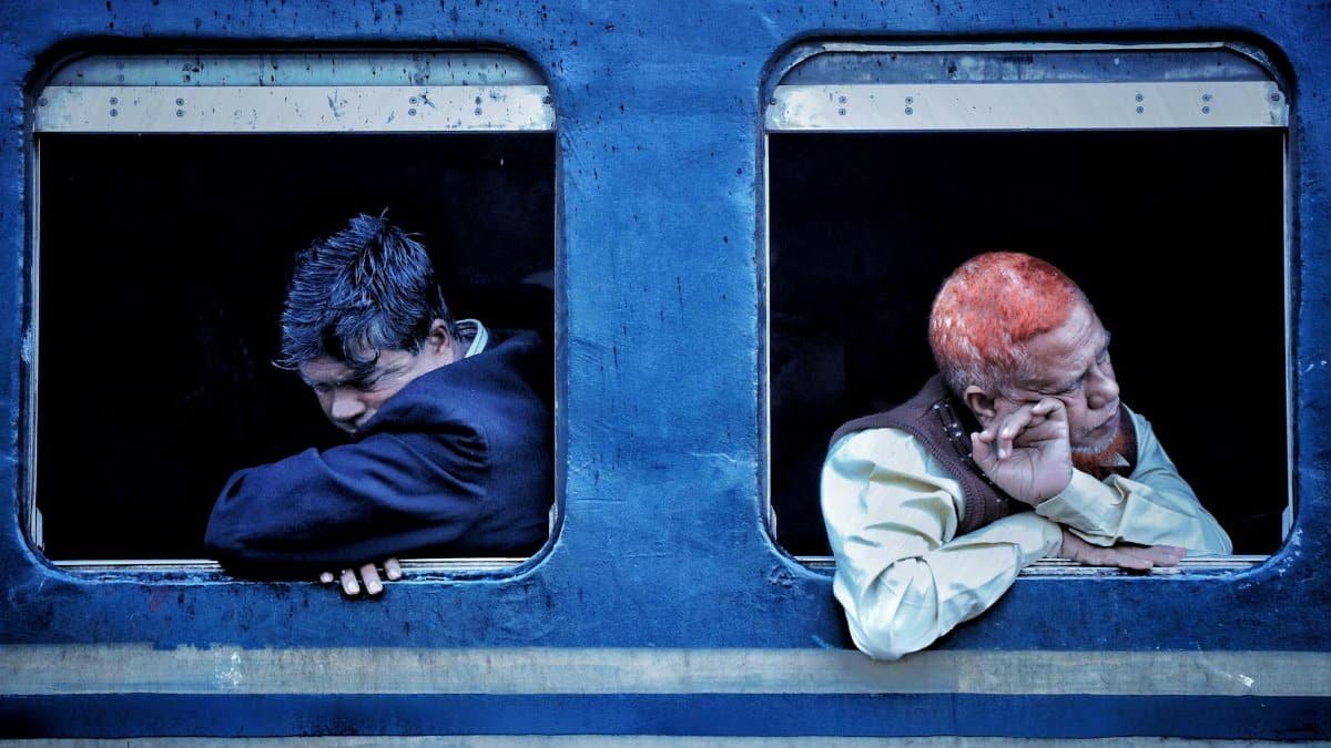 Two men resting on a train, gazing out the windows during their journey.