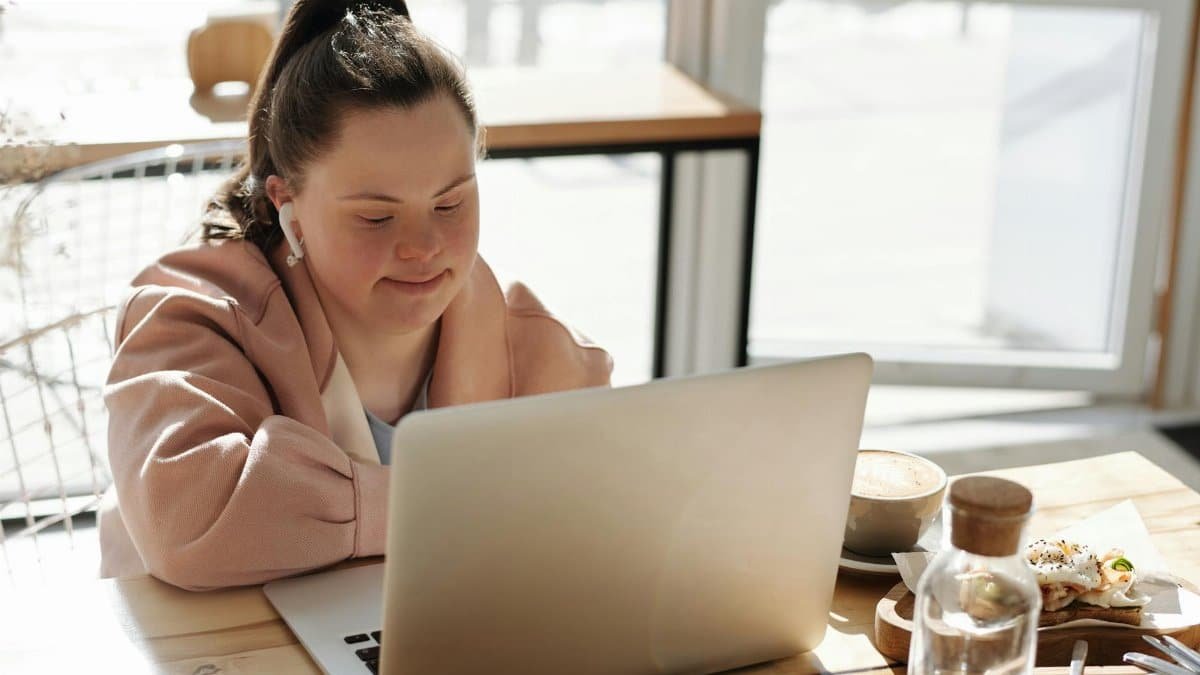 Young woman with Down syndrome using a laptop at home, enjoying coffee. Perfect for lifestyle and technology themes.
