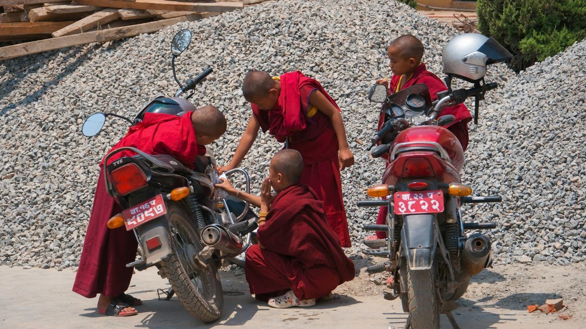 Young Buddhist monks in red robes working on motorcycles outdoors. Captures cultural and religious daily life.