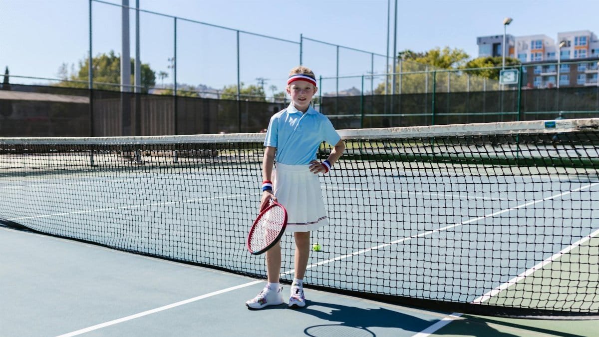 A young girl in sportswear poses with a tennis racket on an outdoor court.