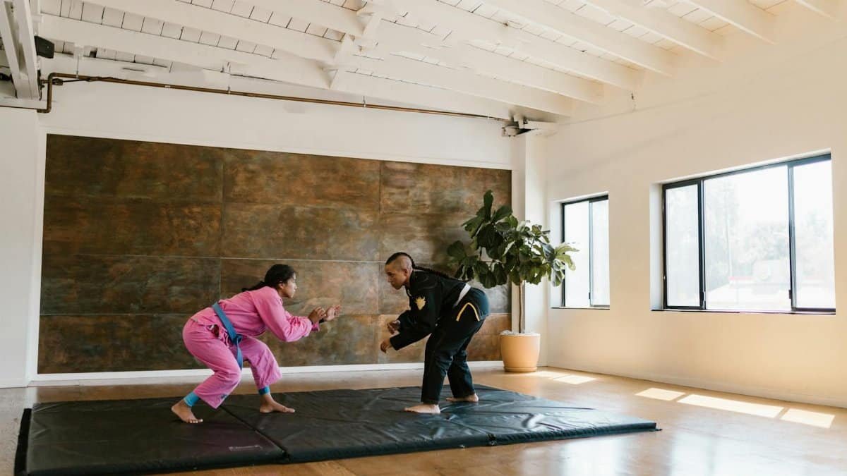 Two martial artists practicing judo techniques on a mat in a brightly lit studio.