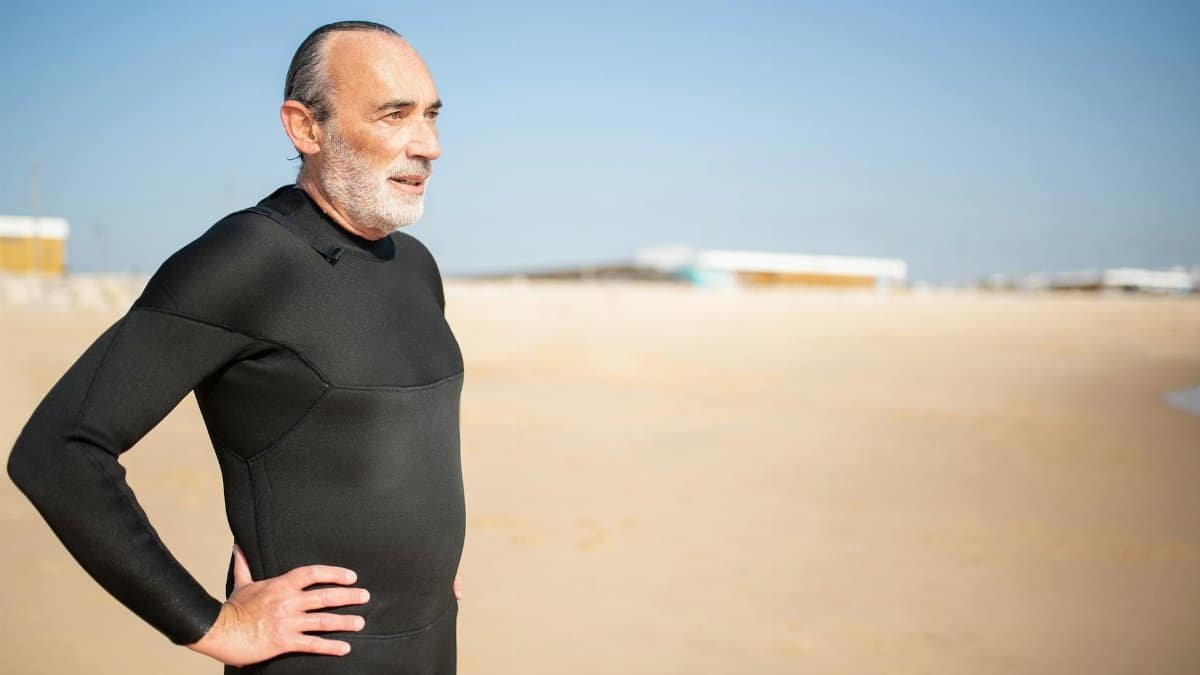 Elderly man in a wetsuit enjoying a sunny day on a Portuguese beach, ready for a swim or surf.