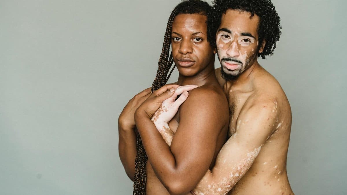 Multiracial homosexual friends cuddling and looking at camera on gray background of studio