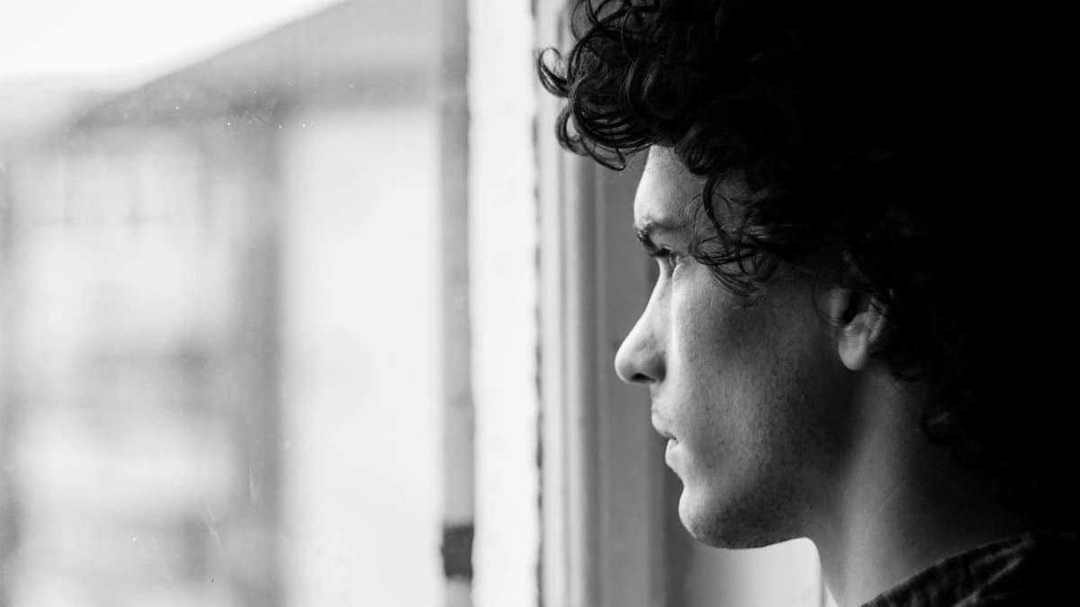 Profile portrait of a young man looking thoughtfully out of a window, in black and white.