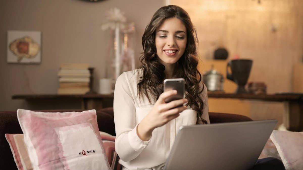 A woman enjoying leisure time using her smartphone and laptop in a cozy living room.