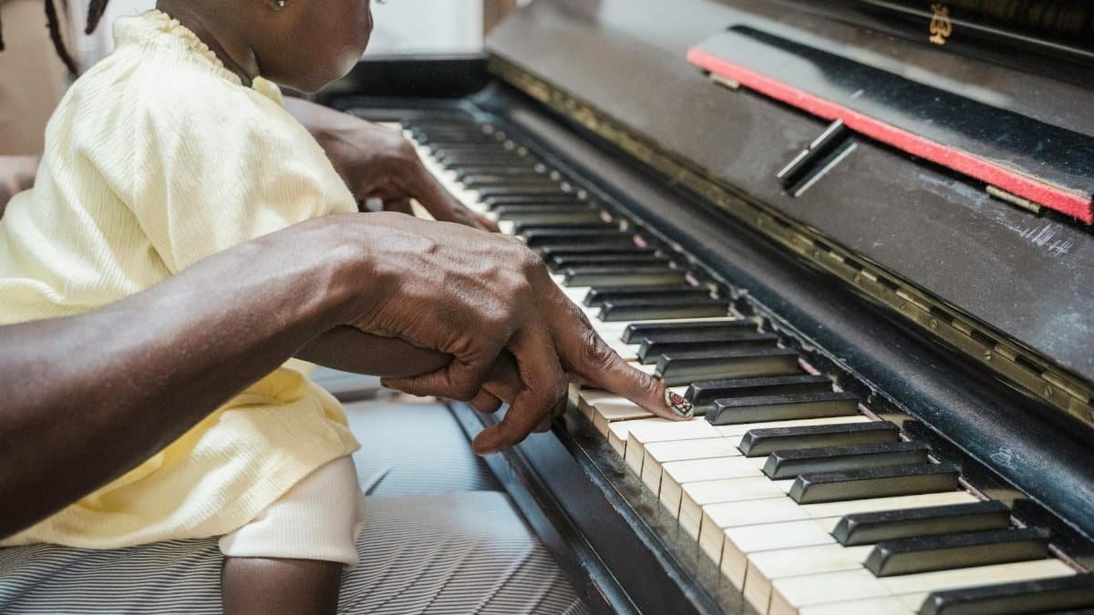 A toddler learns to play piano with guidance from a parent, fostering a love for music.