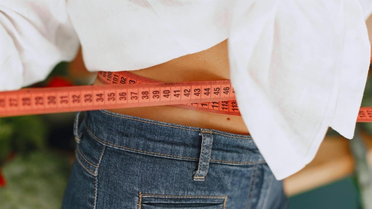 Close-up image of a woman measuring her waist with a tape measure, promoting fitness and health goals.