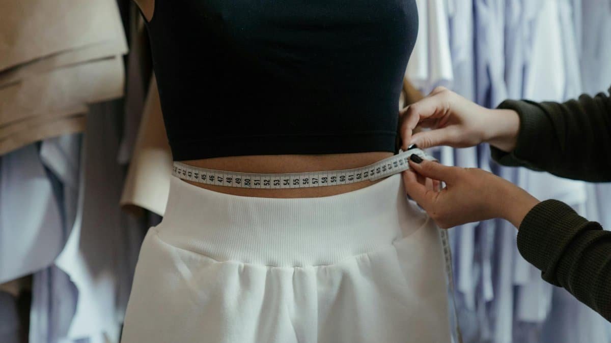Detailed view of a tailor measuring a client's waist in a clothing workshop, focusing on precision.