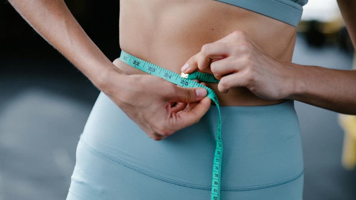Close-up of a woman measuring her waist with a tape in a fitness setting.
