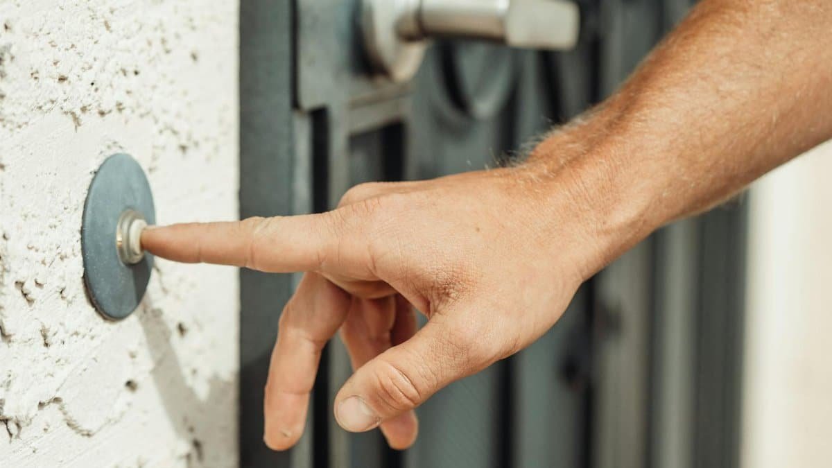 A close-up image of a hand pressing a doorbell outside a modern residential door.