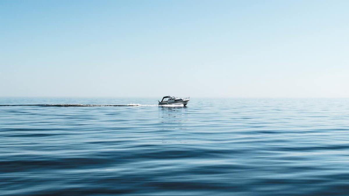 A lone boat cruising through calm ocean waters under a clear blue sky.