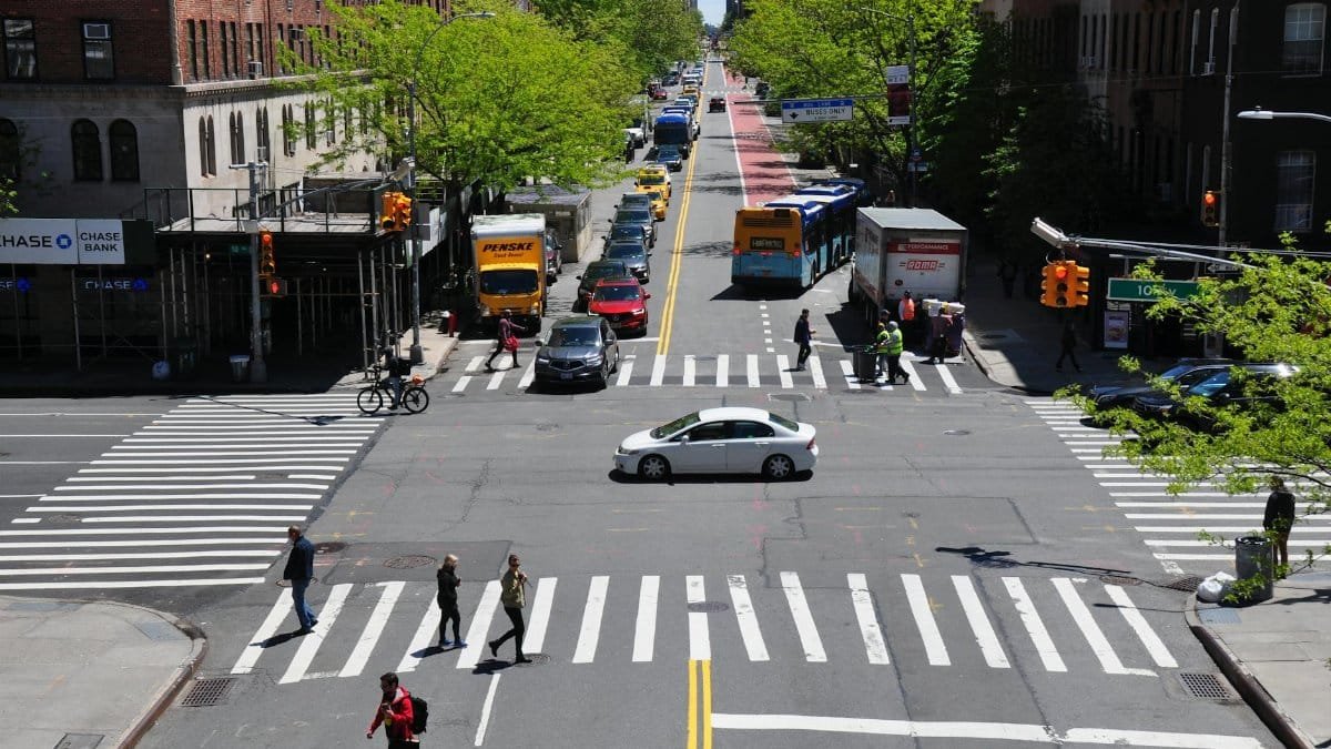 A bustling New York City intersection with cars, buses, and pedestrians on a sunny day.
