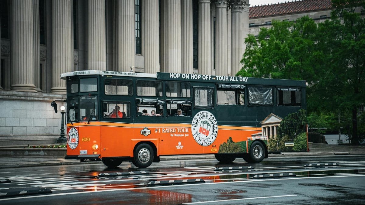 A vibrant tour bus navigating wet streets in front of historical architecture in Washington DC.