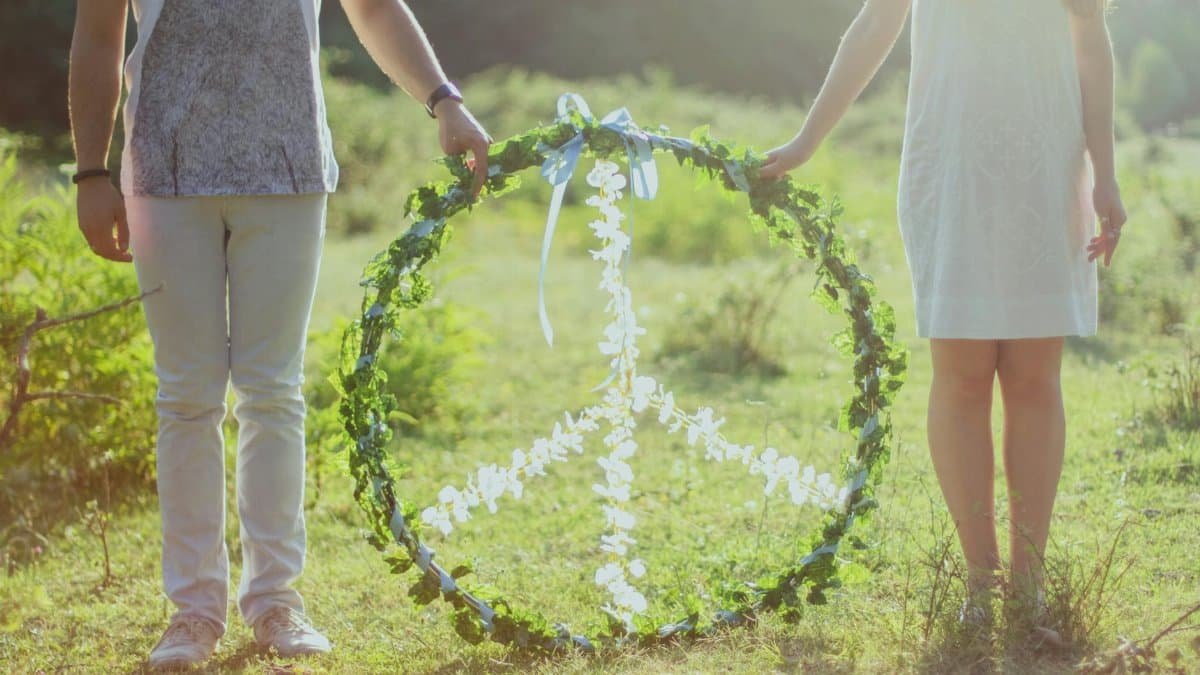 A couple holding a floral peace symbol outdoors in a sunny meadow.